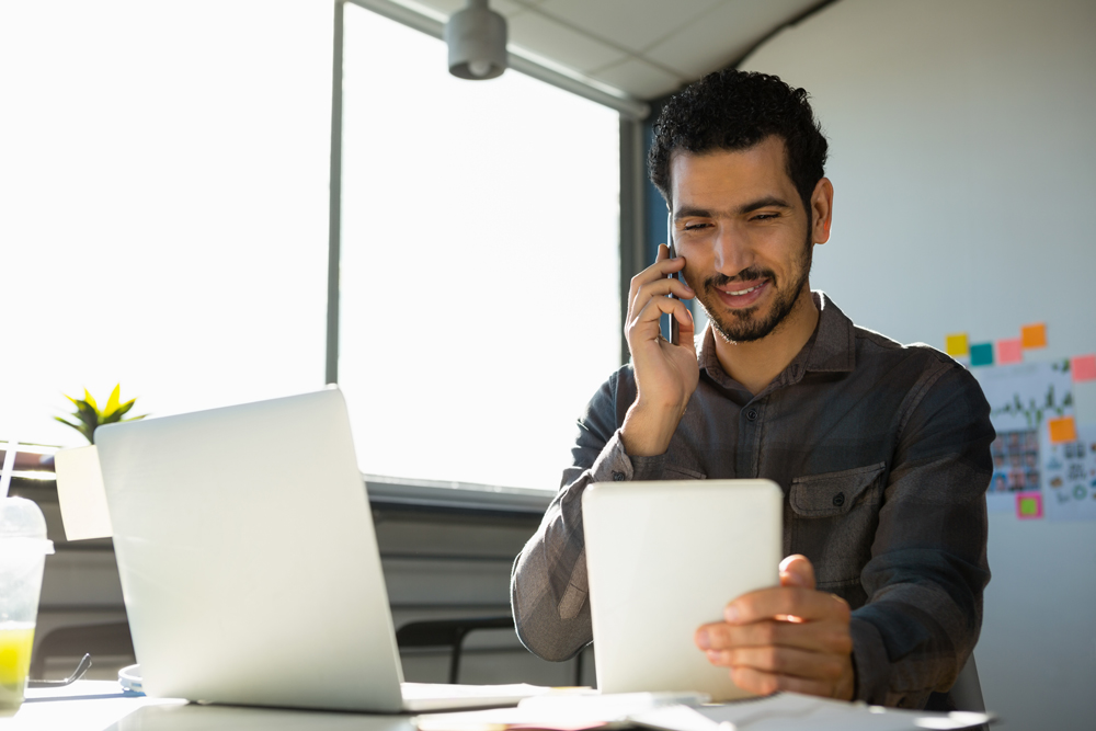 Office worker taking landline calls on his mobile whilst looking at hist tablet device